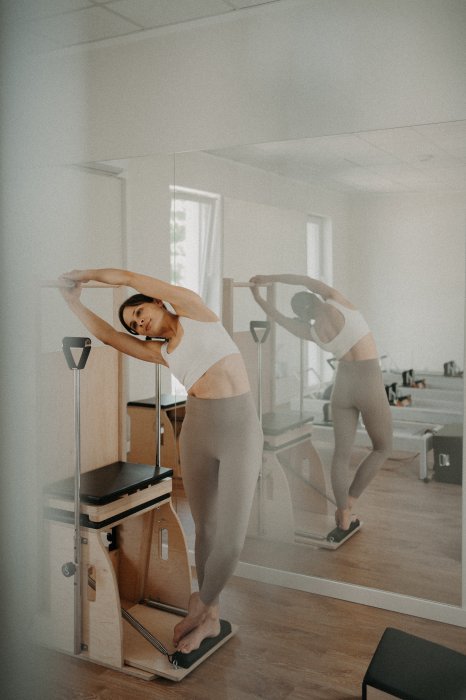 Instruktorka pilates w bocznym rozciągnięciu przy electric chair w jasnej sali Holica Studio
